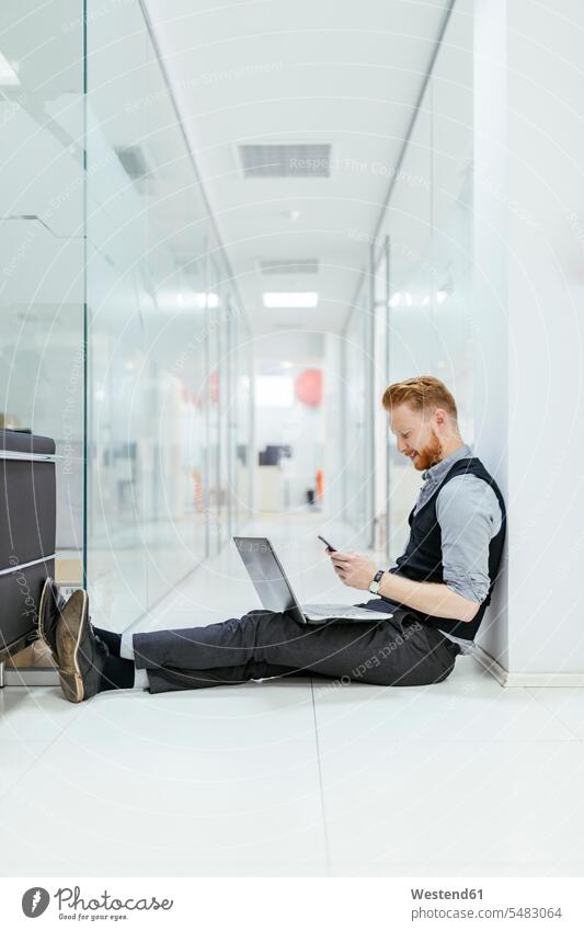 Geschäftsmann im Büro, der auf dem Boden sitzt und einen Laptop benutzt Smartphone iPhone Smartphones Böden Boeden SMS Textnachricht sitzen sitzend lesen