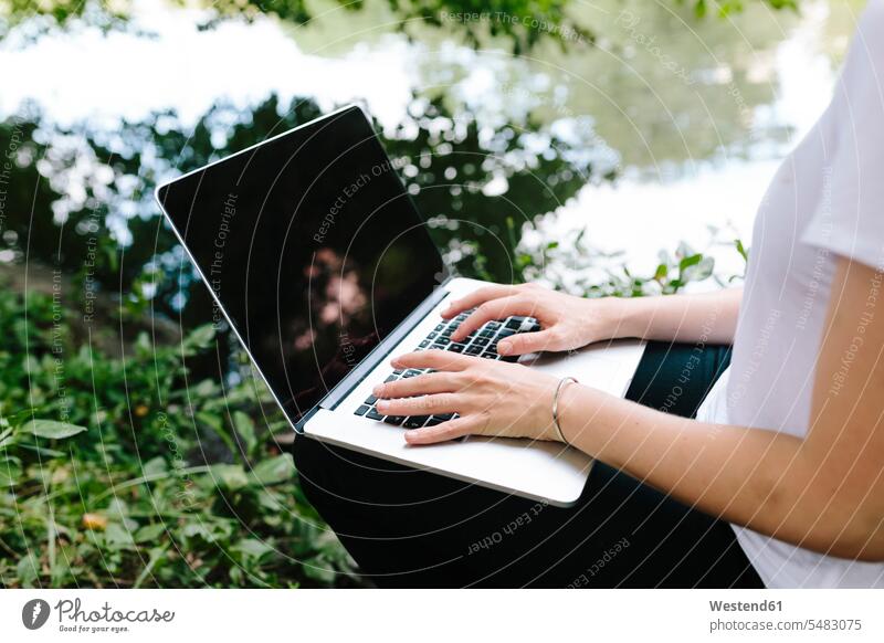 Nahaufnahme einer Frau, die am Seeufer im Park mit einem Laptop sitzt Notebook Laptops Notebooks weiblich Frauen sitzen sitzend Parkanlagen Parks Computer