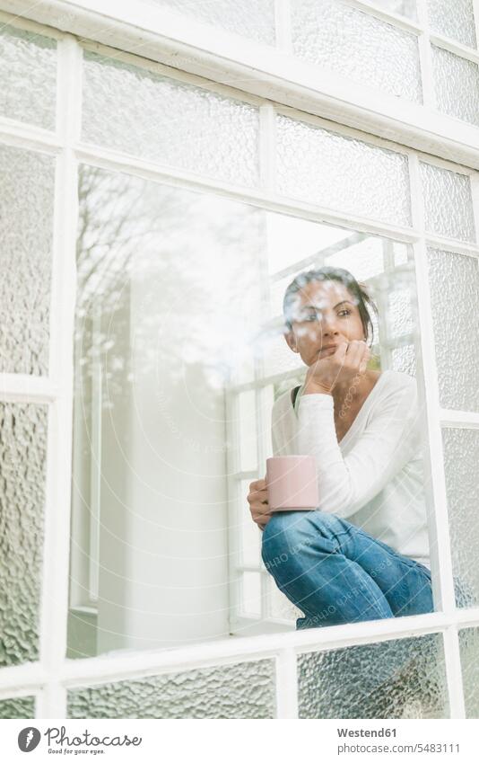 Nachdenkliche Frau mit einer Tasse Kaffee, die aus dem Fenster schaut schauen sehend weiblich Frauen ernst Ernst Ernsthaftigkeit ernsthaft Erwachsener erwachsen