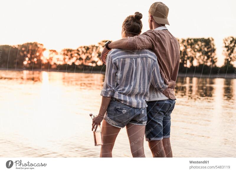 Junges Paar beobachtet den Sonnenuntergang über einem Fluss Aussicht Ausblick Ansicht Überblick stehen stehend steht Sonnenuntergänge Pärchen Paare