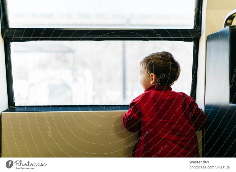 Rückenansicht eines kleinen Jungen auf seiner ersten Zugfahrt mit Blick durchs Fenster Buben Knabe Knaben männlich Freizeitkleidung casual Freizeitbekleidung