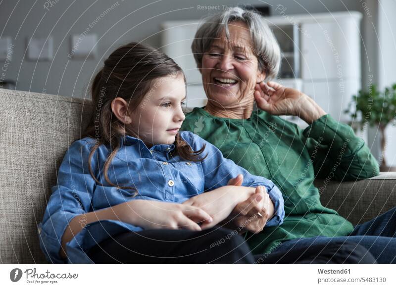 Großmutter und ihre Enkelin sitzen zu Hause zusammen auf der Couch Europäer Kaukasier Europäisch kaukasisch Grossmutter Oma Grossmama Großmütter Omi