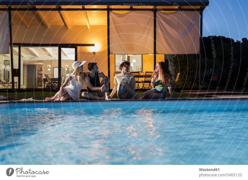 Vier Freunde entspannen in der Abenddämmerung am Pool sitzen sitzend sitzt Swimmingpool Swimmingpools Schwimmbecken Swimming Pool Swimming Pools Freundschaft