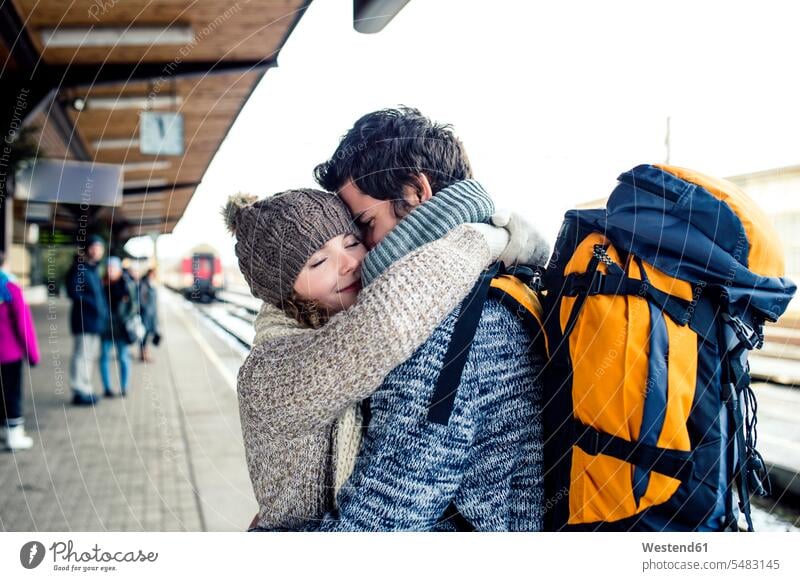 Lächelndes junges Paar umarmt sich auf dem Bahnsteig Bahnhof Bahnhöfe Bahnhoefe lächeln Freizeitkleidung casual Freizeitbekleidung Zugbahnsteig Zugbahnsteige