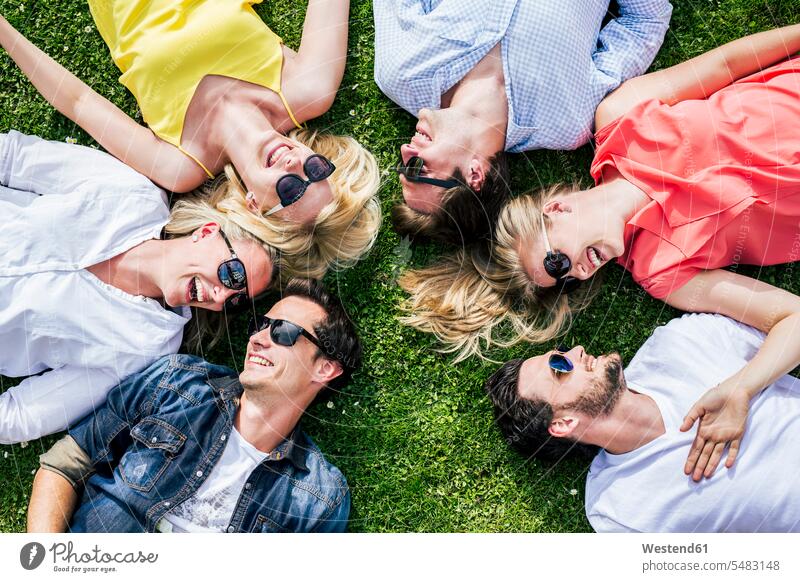 Glückliche Freunde mit Sonnenbrille liegen zusammen auf der Wiese Vergnügen genießen freuen Amüsement Freude vergnügt amusieren lächeln Zusammengehörigkeit