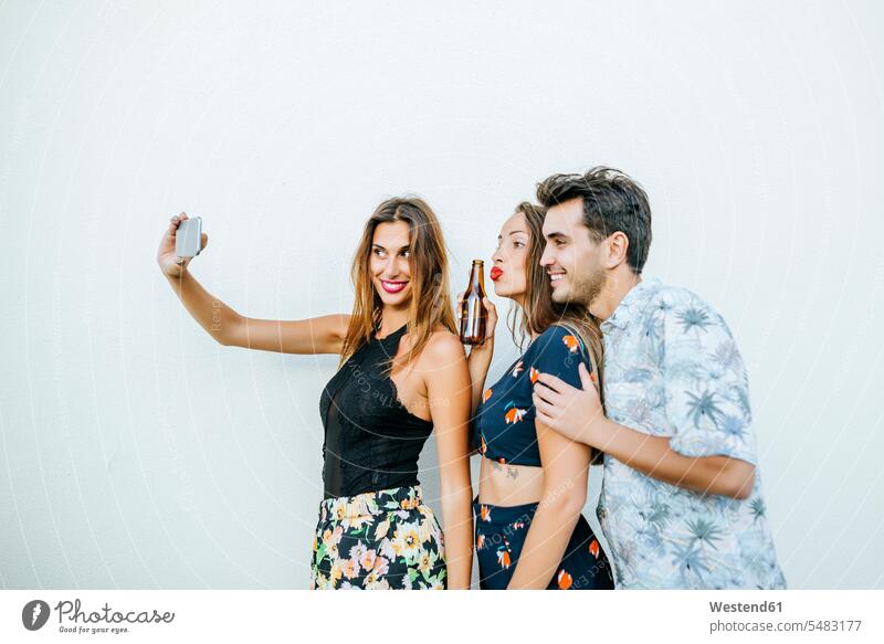 Freunde machen ein Selfie mit Smartphone vor einer weißen Wand Spaß Spass Späße spassig Spässe spaßig Handy Mobiltelefon Handies Handys Mobiltelefone Selfies