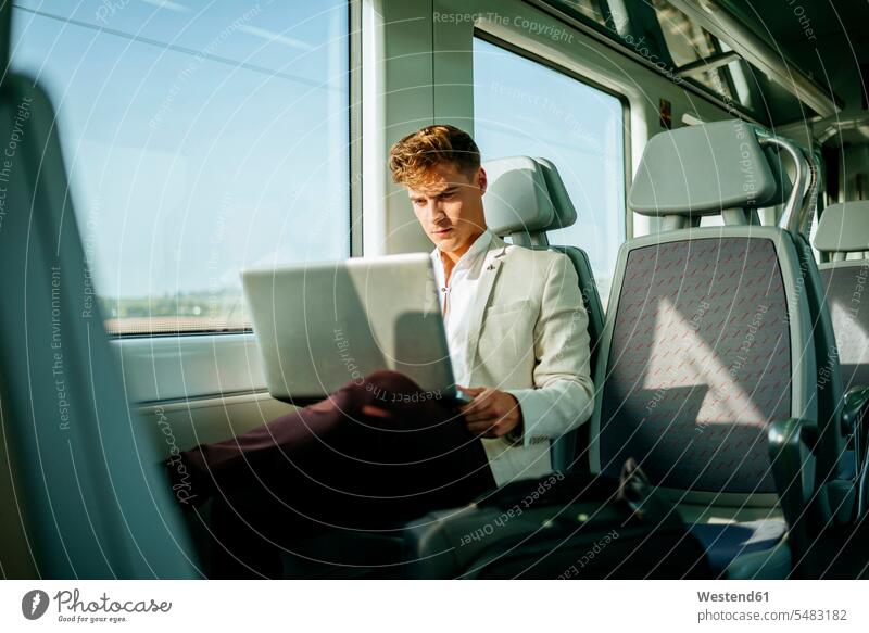 Junger Mann mit einem Laptop im Zug Notebook Laptops Notebooks reisen verreisen Geschäftsmann Businessmann Businessmänner Geschäftsmänner Männer männlich Bahnen