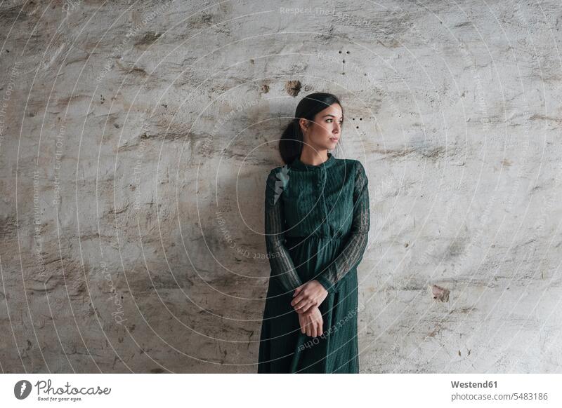Junge Frau in grünem Kleid, vor der Wand stehend jung ernst Ernst Ernsthaftigkeit ernsthaft Kleider traurig Mauer Mauern weiblich Frauen Emotion Gefühl