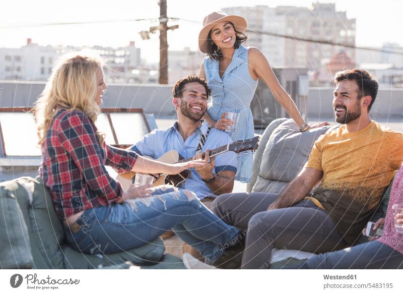 Freunde feiern eine Party auf dem Dach und spielen Gitarre Dachterrasse Dachterrassen Spaß Spass Späße spassig Spässe spaßig Sofa Couches Liege Sofas Gitarren