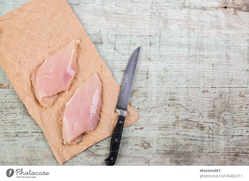 Hühnerbrust auf braunem Papier und einem Messer Draufsicht Vogelperspektive von oben Aufsicht aufgeschnitten Scheibe angeschnitten Stück Stücke Scheiben roh
