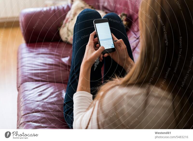 Junge Frau auf der Couch Textnachrichten Handy Mobiltelefon Handies Handys Mobiltelefone Sofa Couches Liege Sofas weiblich Frauen Telefon telefonieren