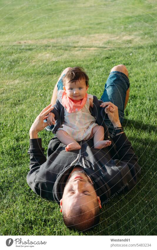 Süßes Mädchen sitzt auf dem Bauch ihres Vaters auf einer Wiese entspannt entspanntheit relaxt Papas Väter Vati Vatis Papis lächeln Baby Babies Babys Säuglinge