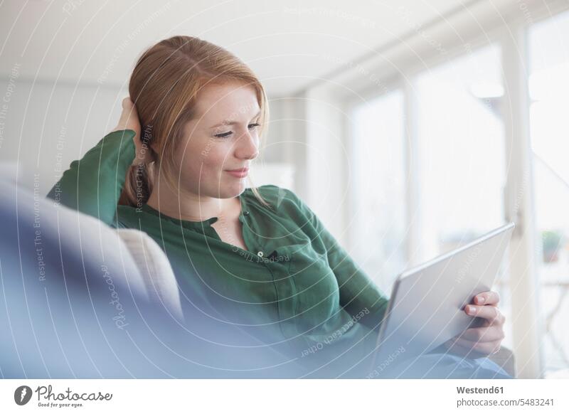 Porträt einer lächelnden jungen Frau mit digitalem Tablet, die sich auf der Couch entspannt Entspannung Entspannen relaxen entspannen aufstützen aufgestuetzt