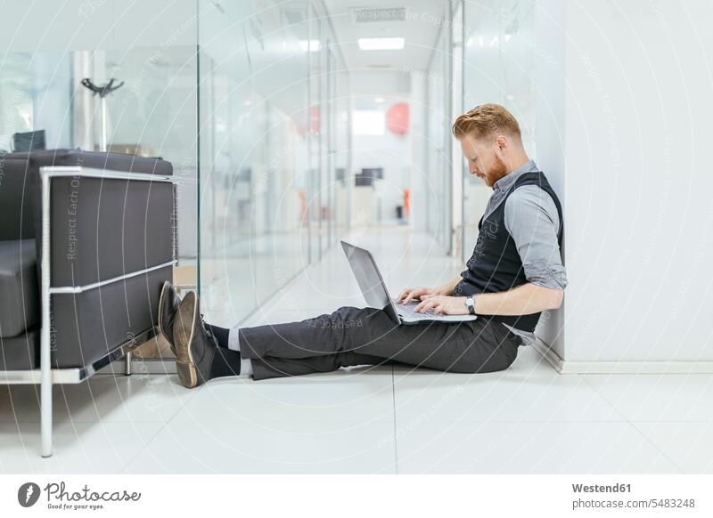 Geschäftsmann im Büro, der auf dem Boden sitzt und einen Laptop benutzt Notebook Laptops Notebooks arbeiten Arbeit sitzen sitzend Office Büros Böden Boeden