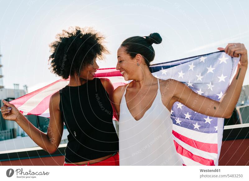 Freundinnen mit US-amerikanischer Flagge auf dem Dach stehend steht lesbisch lächeln Unbeschwert Sorglos Spaß Spass Späße spassig Spässe spaßig