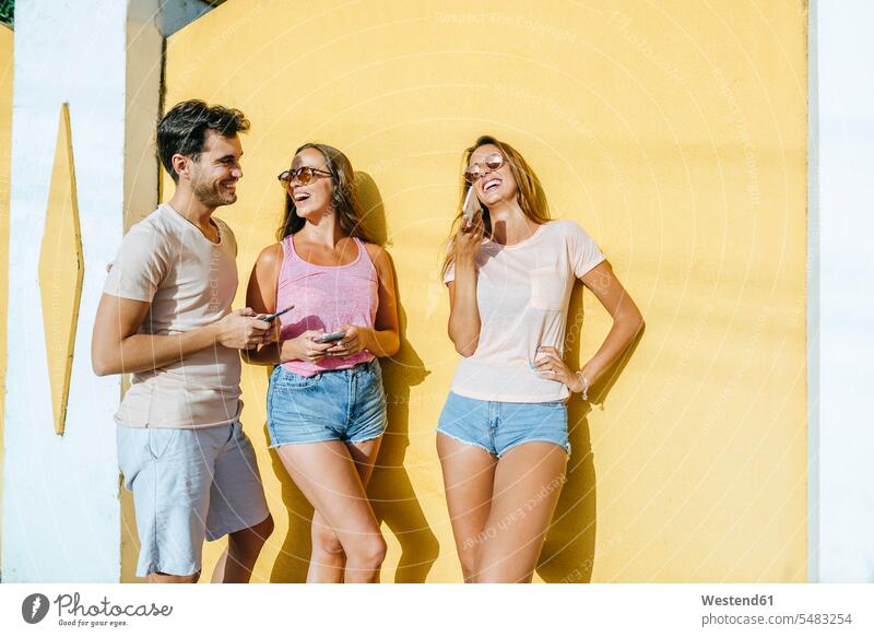 Drei glückliche Freunde mit Mobiltelefonen im Freien lachen Handy Handies Handys Spaß Spass Späße spassig Spässe spaßig positiv Emotion Gefühl Empfindung