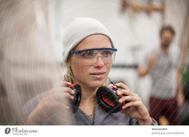Frau trägt Schutzbrille und Ohrenschützer im Workshop Werkstatt Werkstätte Werkstaette Werkstaetten Werkstätten arbeiten Arbeit Handwerk Gewerbe weiblich Frauen