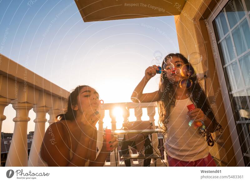 Teenagermädchen und ihre kleine Schwester blasen Seifenblasen auf dem Balkon entspannt entspanntheit relaxt glücklich Glück glücklich sein glücklichsein