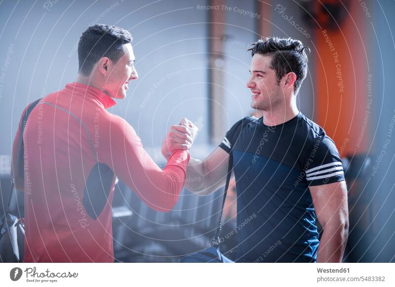 Zwei junge Männer schütteln sich in der Turnhalle die Hand Freunde trainieren lächeln Fitnessstudio Fitnessclubs Fitnessstudios Freundschaft Kameradschaft fit