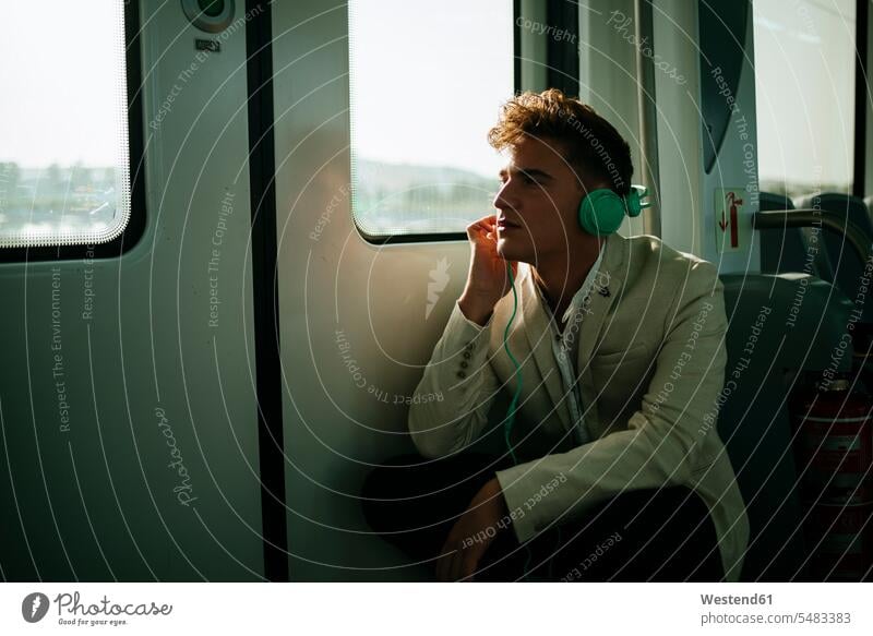 Junger Mann hört Musik in einem Zug hören hoeren Bahnen Züge Männer männlich reisen verreisen Kopfhörer Kopfhoerer Verkehrswesen Transportwesen Erwachsener