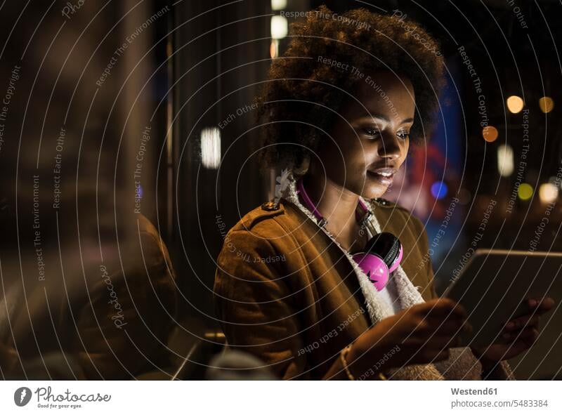 Junge Frau mit Kopfhörern benutzt Tabletten, während sie an der Straßenbahnhaltestelle wartet weiblich Frauen Tablet Computer Tablet-PC Tablet PC iPad