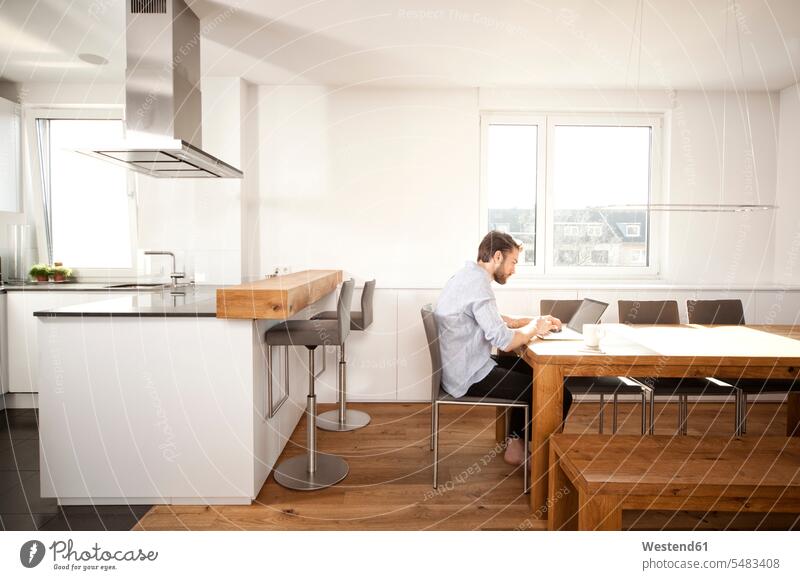 Mann sitzt mit Laptop am Tisch in seiner offenen Küche Erreichbarkeit verfügbar Verfügbarkeit erreichbar Verfuegbarkeit verfuegbar sitzen sitzend Lifestyle