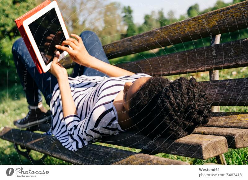 Junge Frau liegt auf Parkbank mit digitalem Tablett Tablet Computer Tablet-PC Tablet PC iPad Tablet-Computer weiblich Frauen Bank Sitzbänke Bänke Sitzbank