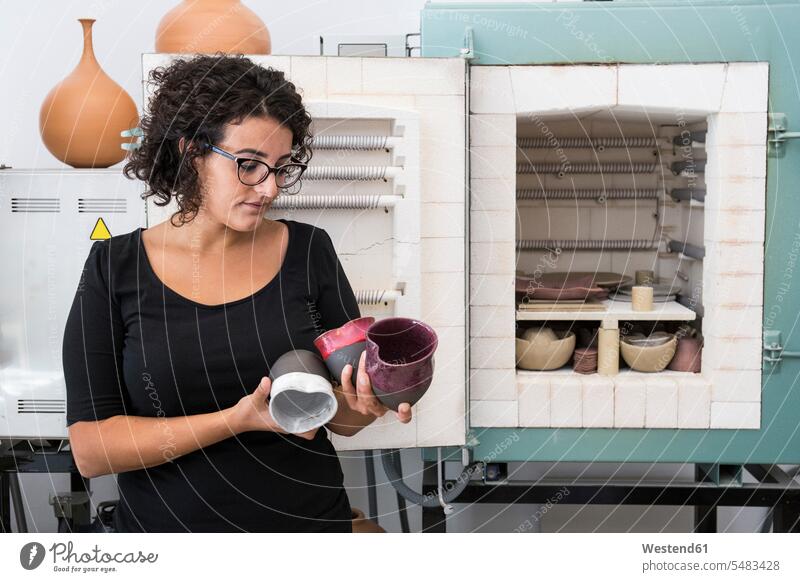 Frau untersucht Tassen aus Keramik in einem Workshop Krug Krüge Kruege Werkstatt Werkstätte Werkstaette Werkstaetten Werkstätten weiblich Frauen ansehen