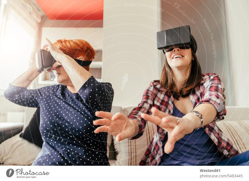 Erwachsene Tochter mit Mutter zu Hause, die eine VR-Brille trägt Töchter virtuell Virtualität Mami Mutti Mütter Mama Frau weiblich Frauen glücklich Glück