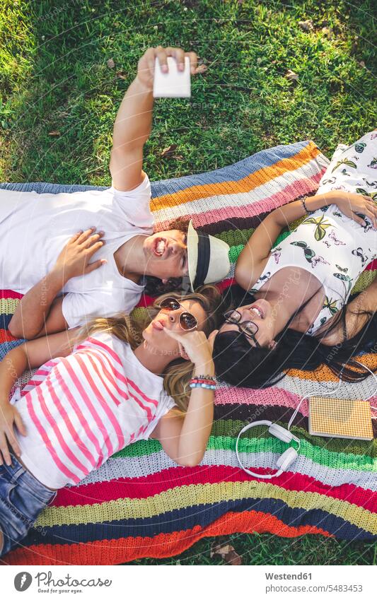Verspielte Freunde liegen auf einer Decke im Park und machen ein Selfie liegend liegt Handy Mobiltelefon Handies Handys Mobiltelefone Selfies entspannt
