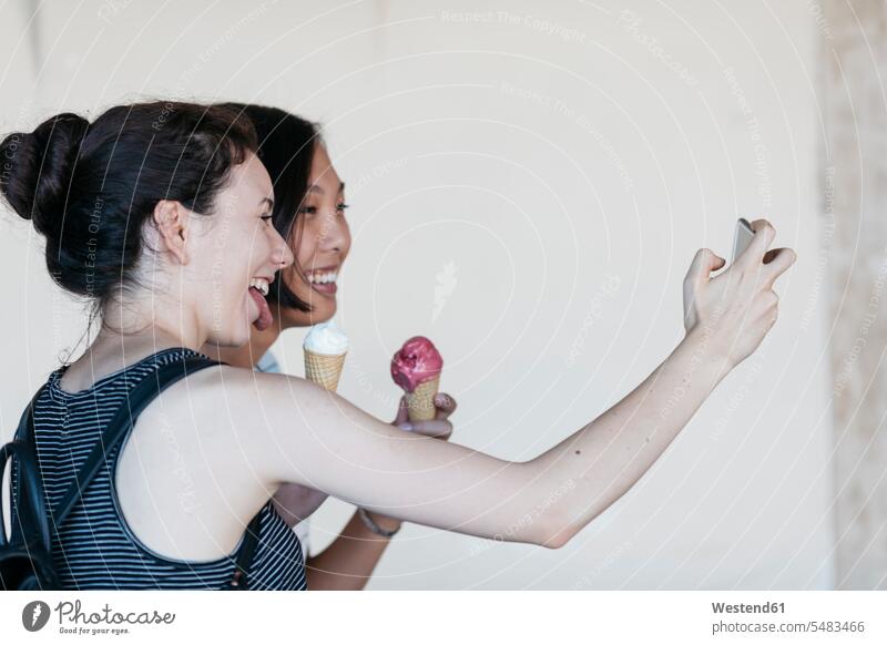 Zwei junge Frauen mit Eistüten machen ein Selfie mit Smartphone Freundinnen Selfies Freunde Freundschaft Kameradschaft essen essend lachen iPhone Smartphones