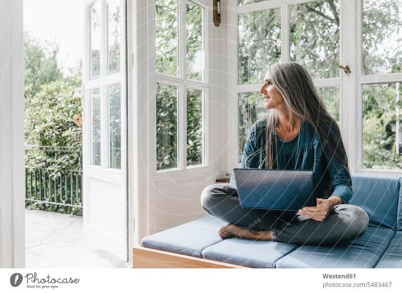 Frau mit Laptop sitzt auf dem Salon im Wintergarten und schaut durch die geöffnete Terrassentür weiblich Frauen Erwachsener erwachsen Mensch Menschen Leute