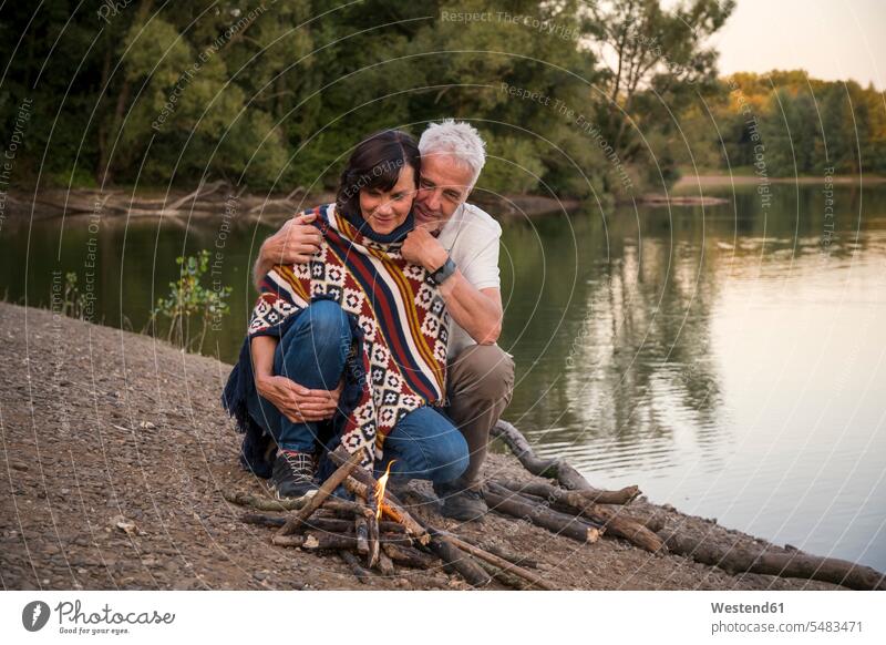 Älteres Ehepaar am Lagerfeuer an einem See entspannt entspanntheit relaxt glücklich Glück glücklich sein glücklichsein Paar Pärchen Paare Partnerschaft Seen