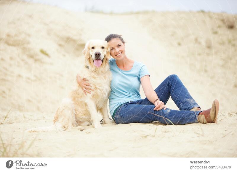 Lächelnde junge Frau mit Hund im Sand lächeln sandig weiblich Frauen Hunde Erwachsener erwachsen Mensch Menschen Leute People Personen Haustier Haustiere Tier