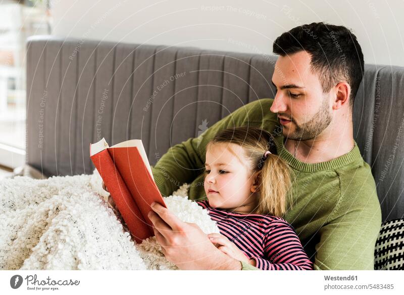 Vater und Tochter lesen zu Hause ein Buch Töchter Papas Väter Vati Vatis Papis Lektüre liegen liegend liegt Kind Kinder Familie Familien Mensch Menschen Leute
