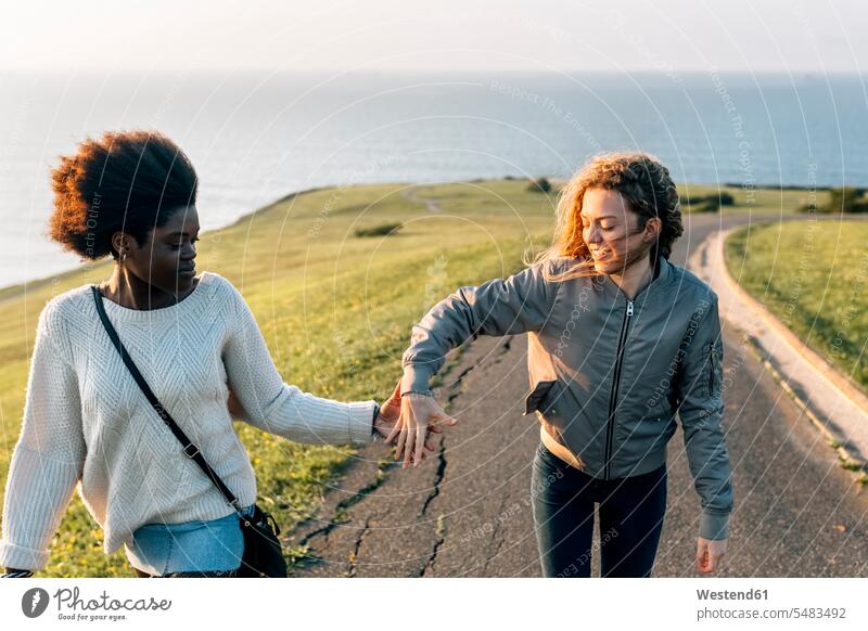 Zwei beste Freunde halten sich beim Spaziergang an der Küste an den Händen glücklich Glück glücklich sein glücklichsein lächeln Frau weiblich Frauen Freundinnen