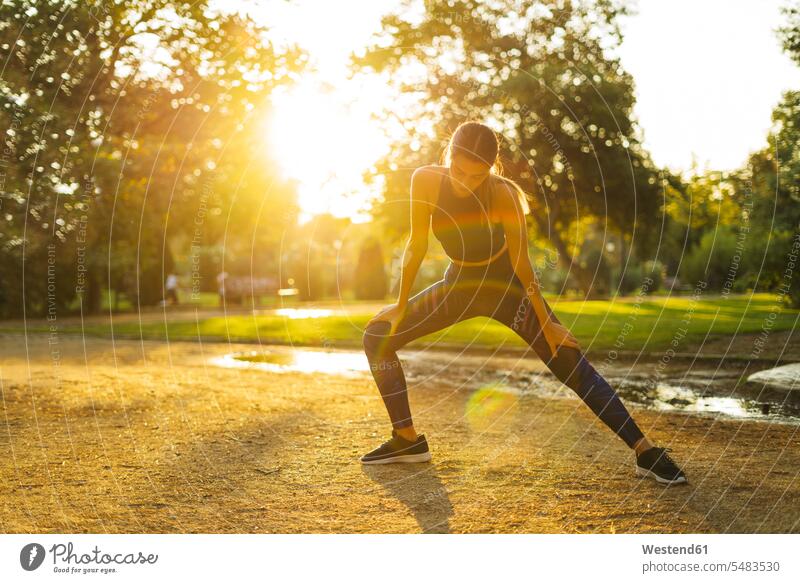 Sportliche junge Frau streckt sich bei Sonnenuntergang im Park dehnen strecken weiblich Frauen Sportlerin Sportlerinnen Erwachsener erwachsen Mensch Menschen