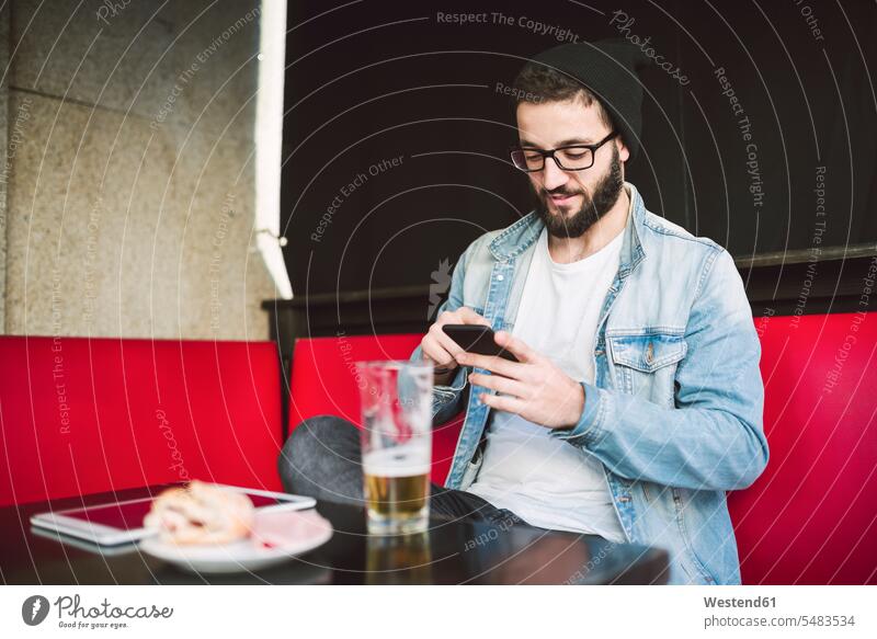 Junger Mann sitzt in einer Kneipe und überprüft Nachrichten Kneipen Smartphone iPhone Smartphones Männer männlich Handy Mobiltelefon Handies Handys