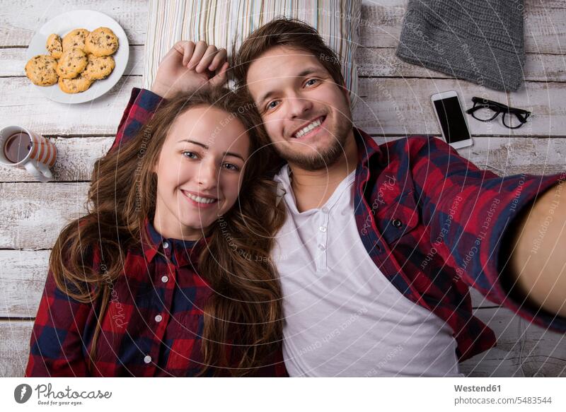 Porträt eines jungen Paares, das auf dem Boden liegt und ein Selfie macht hölzern braune Haare braunhaarig brünett braunes Haar Teller Entspannung relaxen