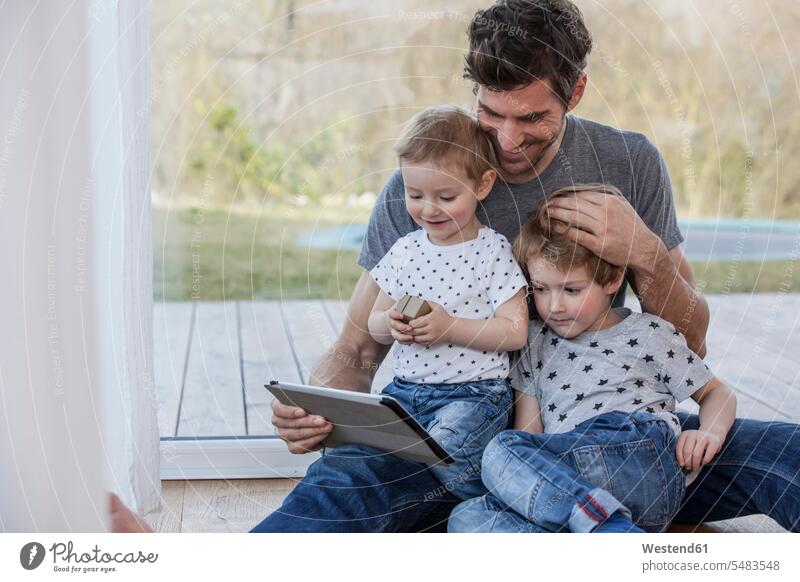 Vater und Söhne sitzen auf dem Boden und benutzen ein digitales Tablett Zufriedenheit zufrieden Mobilität mobil Verbindung verbunden verbinden Anschluss