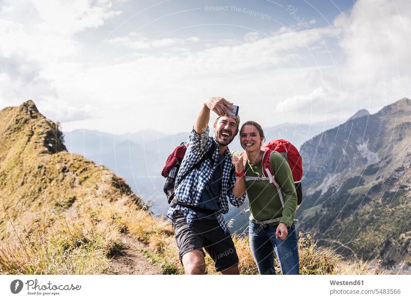 Deutschland, Bayern, Oberstdorf, glückliches Paar bei einem Selfie auf einem Bergkamm Pärchen Paare Partnerschaft Gebirge Berglandschaft Gebirgslandschaft