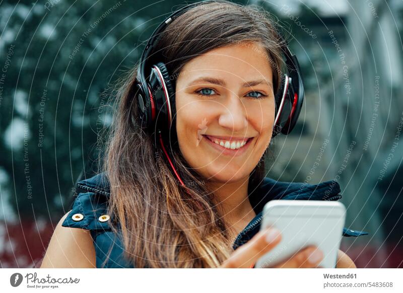 Porträt einer lächelnden jungen Frau mit Kopfhörer und Handy in der Stadt Musik Mobiltelefon Handies Handys Mobiltelefone weiblich Frauen Kopfhoerer hören
