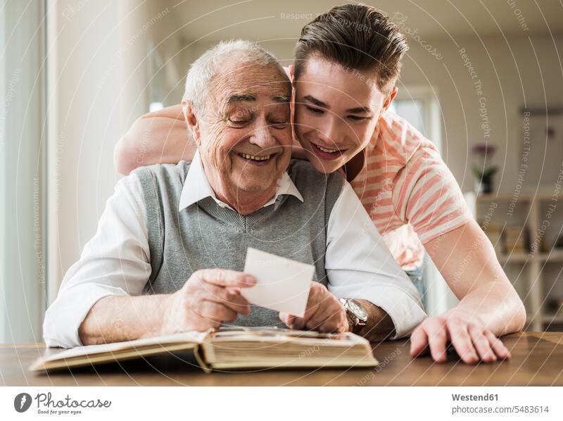 Großvater und Enkel schauen sich gemeinsam alte Fotografien an Freizeitbeschäftigung Freizeitbeschaeftigung Vertrautheit Vertrauen vertrauen Portrait Porträts