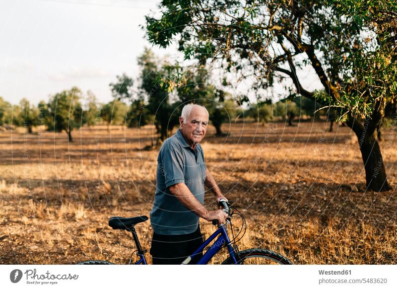 Älterer Mann mit Fahrrad auf einem Feld Männer männlich Erwachsener erwachsen Mensch Menschen Leute People Personen Senior ältere Männer älterer Mann Senioren