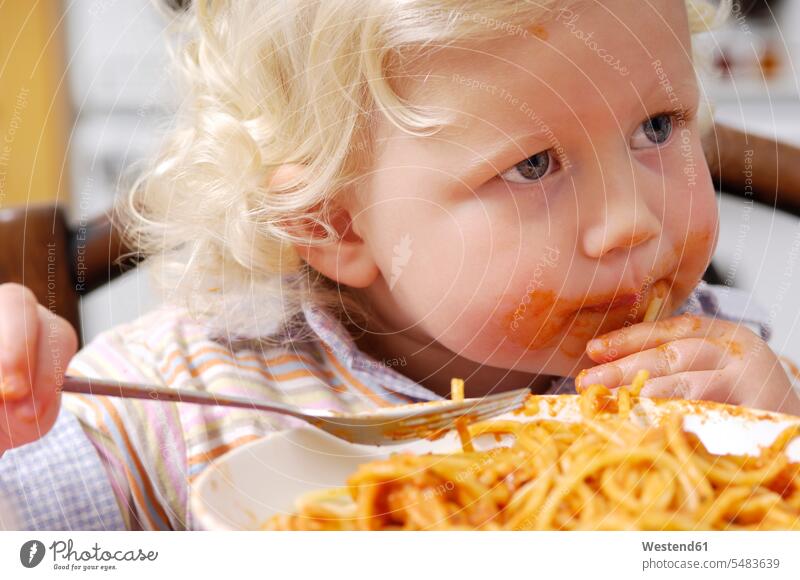Porträt eines kleinen blonden Mädchens, das Spaghetti mit Tomatensauce isst Teller verschmiert Sauerei Unordnung dreckig unordentlich verschmutzt Seitenblick