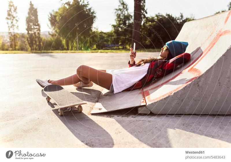 Junge Frau mit Skateboard und Handy in einem Skatepark entspannt entspanntheit relaxt Rollbretter Skateboards liegen liegend liegt Mobiltelefon Handies Handys