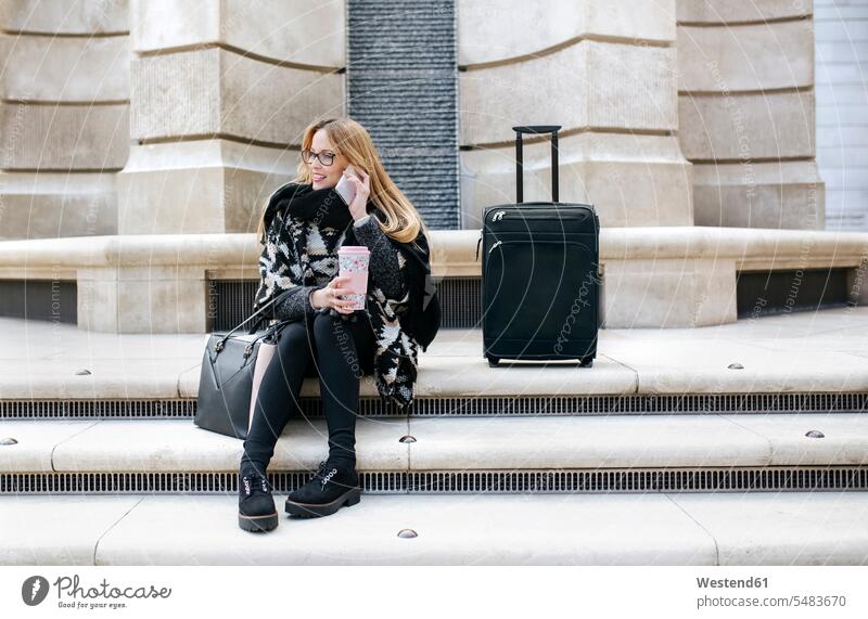 Junge Frau mit Gepäck am Handy auf der Treppe Gebäude blond blonde Haare blondes Haar Poncho Verbindung verbunden verbinden Anschluss Telekommunikation Trolley