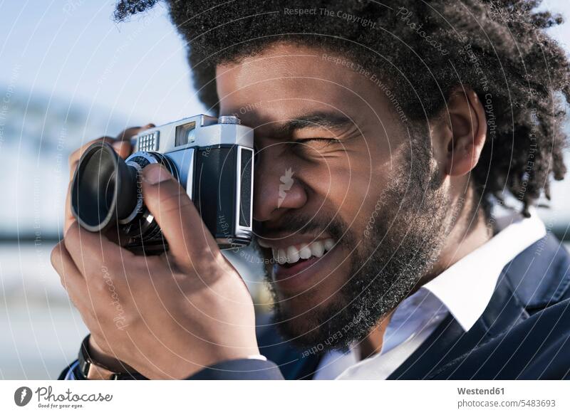 Nahaufnahme eines lächelnden Mannes, der mit einer Oldtimer-Kamera fotografiert Männer männlich fotografieren Fotoapparat Fotokamera Erwachsener erwachsen