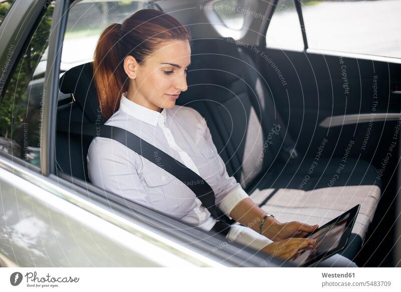 Geschäftsfrau, die auf dem Rücksitz eines Autos sitzt und ein Tablett benutzt Tablet Computer Tablet-PC Tablet PC iPad Tablet-Computer Geschäftsfrauen