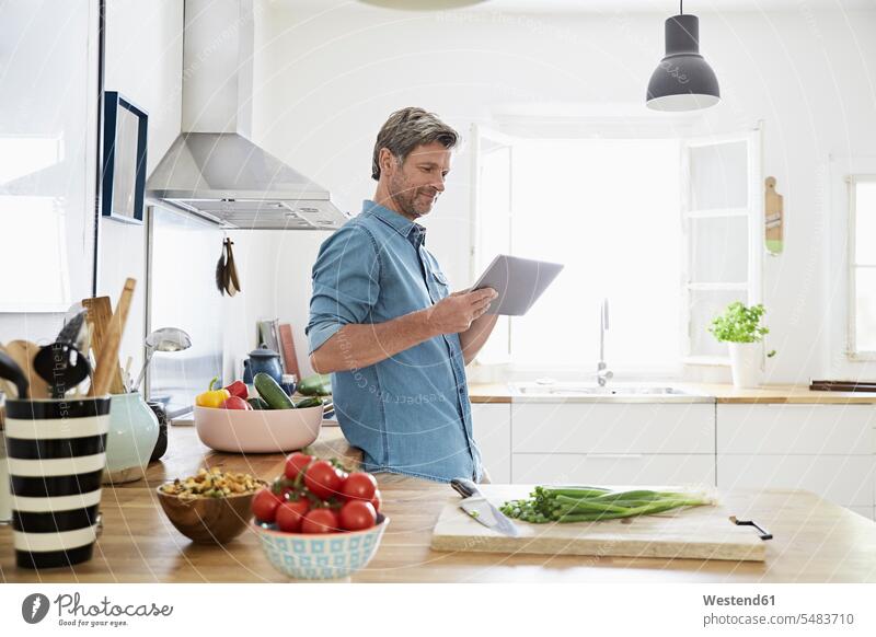 Reifer Mann in seiner Küche liest Rezept auf seinem digitalen Tablett Männer männlich Zuversicht Zuversichtlich Selbstvertrauen selbstbewusst Vertrauen kochen